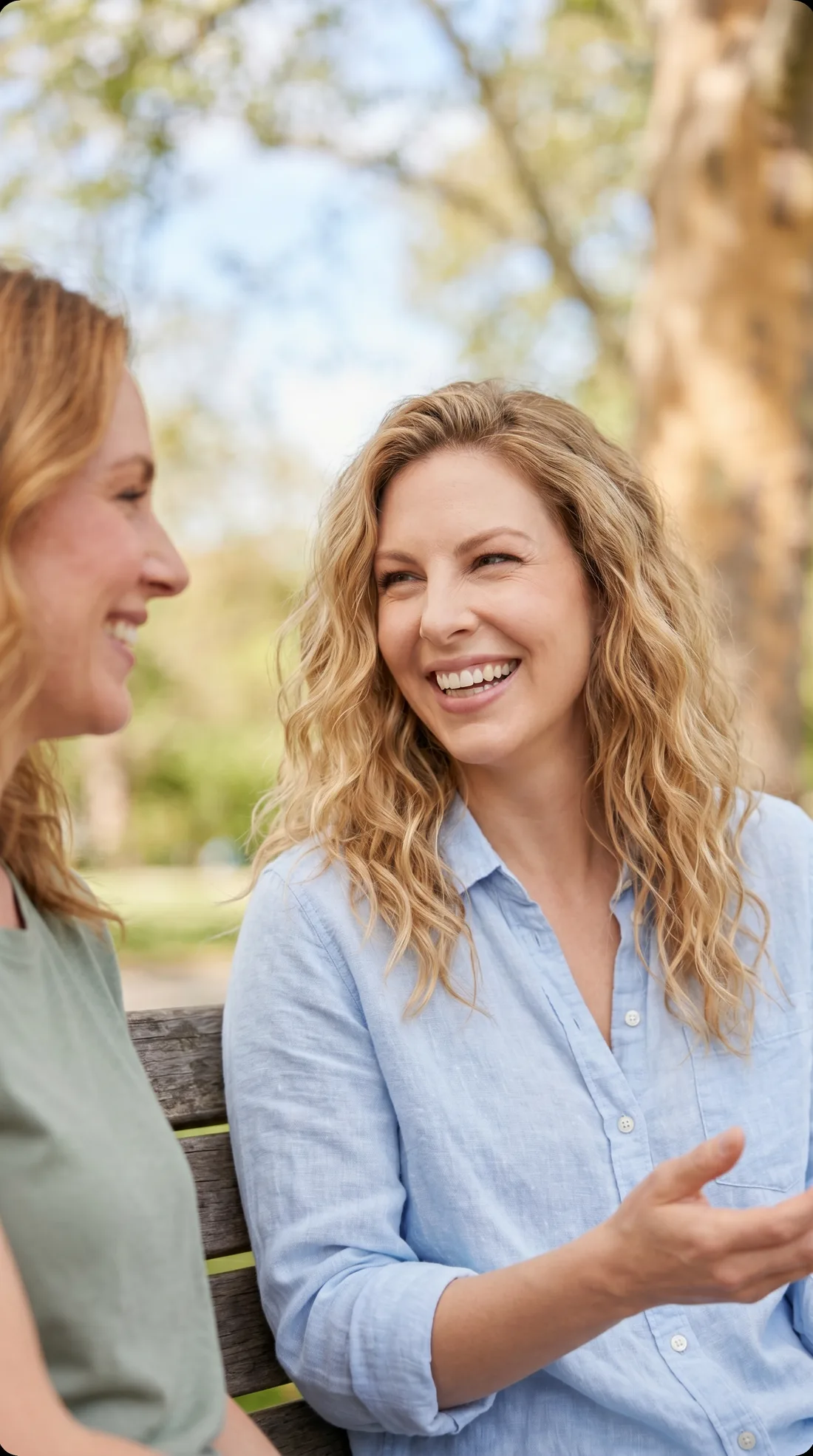 Two women smiling and talking together on a park bench