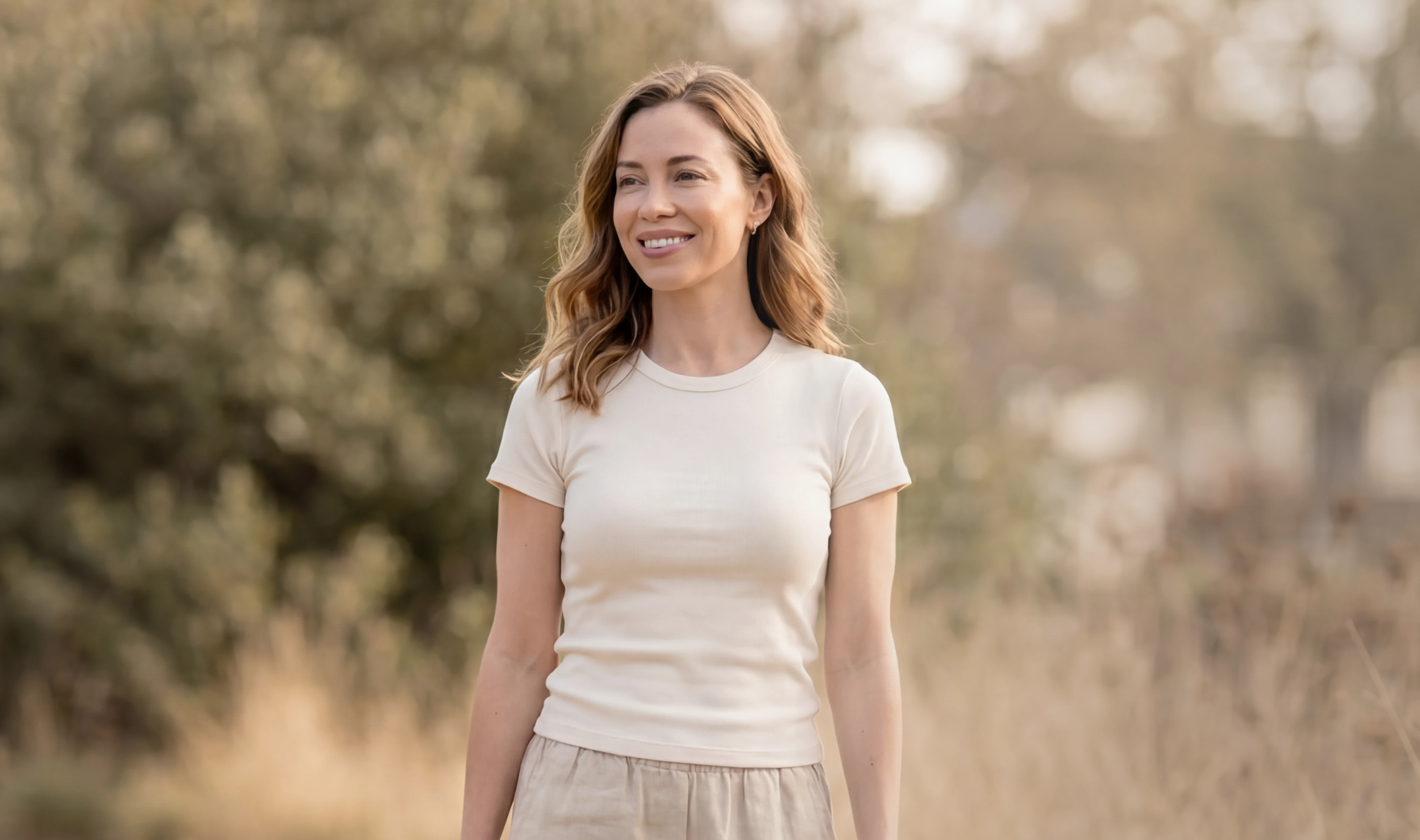A woman in an olive blazer walking through a sunlit park