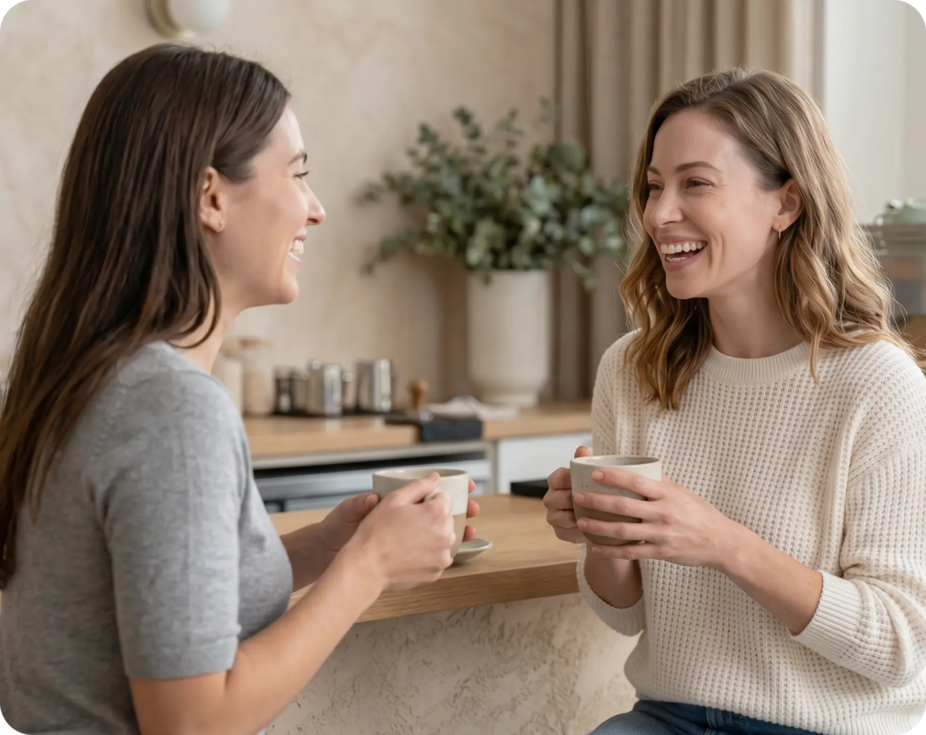 Two women laughing together over coffee in a kitchen